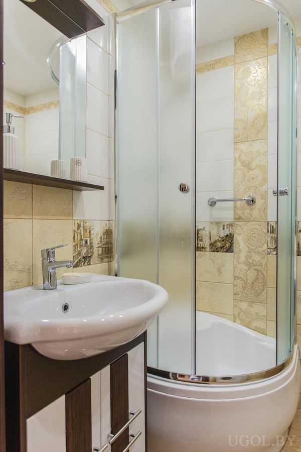 Угловая душевая с прозрачными дверцами, тёмная тумба под раковиной, плитка с архитектурными мотивами.