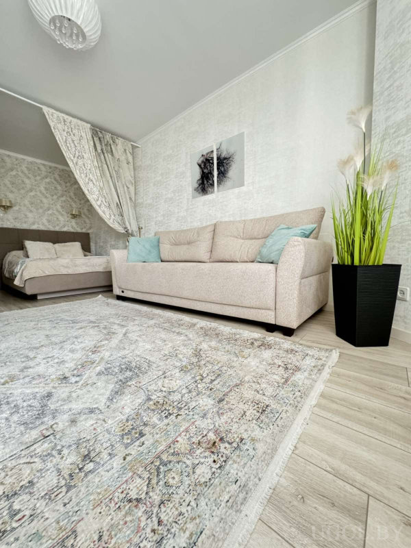 Бежевый диван с голубыми подушками, ковёр с узором, кровать за шторой, панно с деревом и декоративная трава в чёрном кашпо.