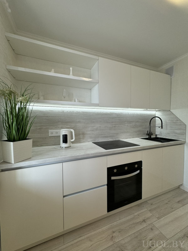 Белые матовые фасады, серый фартук с древесной текстурой, чёрная варочная панель, духовка и раковина с высоким изливом.