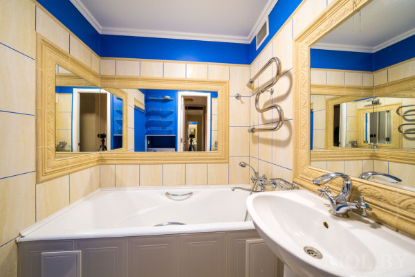 Комната с ванной, умывальником, зеркалами, полотенцесушителем и отражением штатива в зеркале.