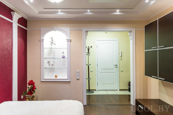 Зона с нишей, стеклянными полками, белой дверью, вешалкой и чёрной тумбой на фоне бордовой стены.