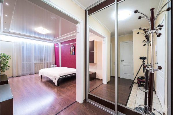 Комната с кроватью, зеркальным шкафом, вешалкой, штативом и тюлем у окна.