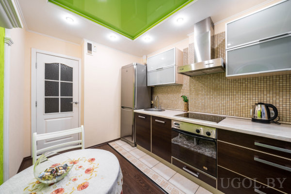 Рабочая зона с плитой, холодильником, столом, зелёным потолком и фартуком из мелкой плитки.
