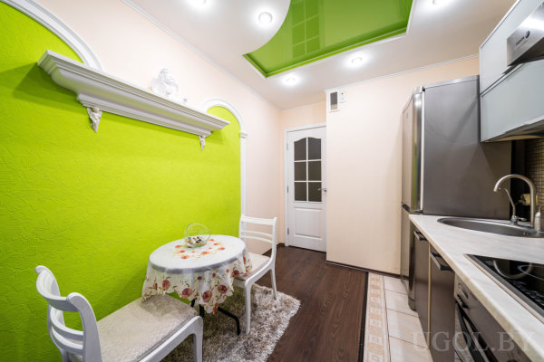 Интерьер с столом, скамьёй, белыми стульями, декоративной полкой и глянцевым потолком.