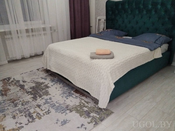 Интерьер с кроватью, подушками, полотенцами, ковром, тюлем и фиолетовой шторой.