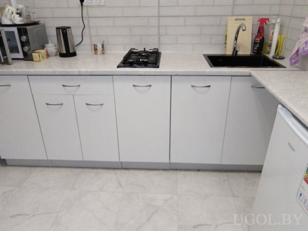 Рабочая зона с плитой, чайником, раковиной, холодильником и белым фартуком.