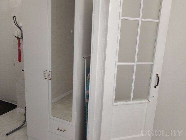 Зона с шкафом, дверью, гладильной доской, вешалкой и белым кафелем на полу.