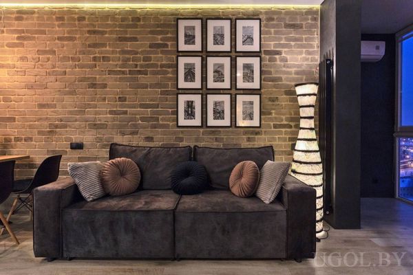 Интерьер с диваном, подушками, настенным декором, торшером и видом на город через окно.