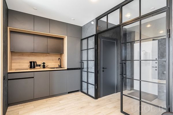 Кухонная зона с серыми шкафами, техникой, деревянным фартуком и перегородкой с видом на душевую.