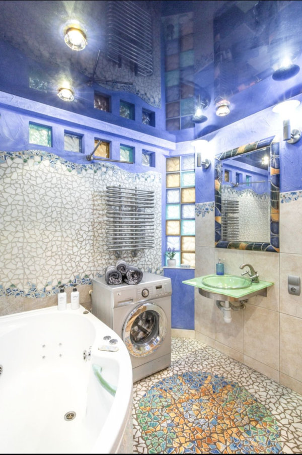 Мозаичные стены, джакузи, зелёная стеклянная раковина, стиральная машина с полотенцами, цветные стеклоблоки и синий потолок.