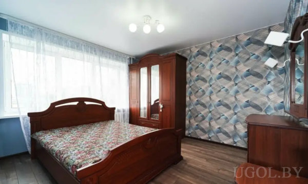 Уютная спальня с цветочным покрывалом, зеркальным шкафом и геометрическими обоями.