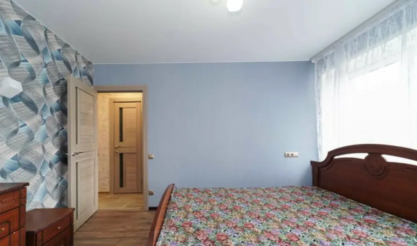 Светлая спальня с абстрактными обоями и открытой дверью в соседнюю комнату.