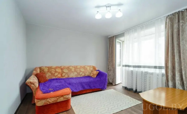 Минималистичный интерьер с цветочным диваном, фиолетовым пледом и деревянным столиком.