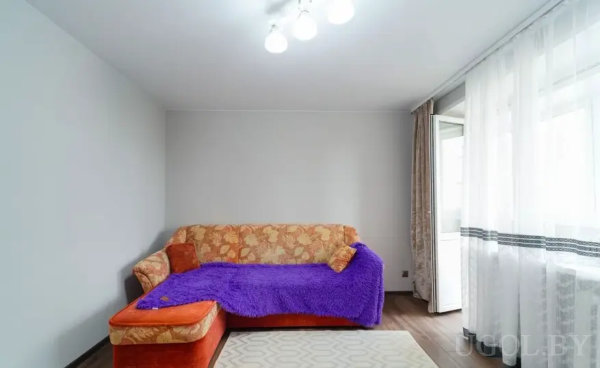 Комната с тёмным полом, белыми стенами и яркими текстильными акцентами.