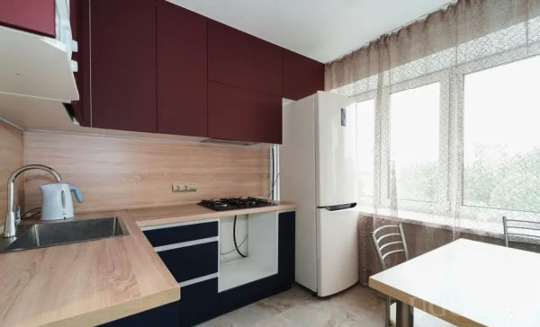 Функциональная кухня с плитой, холодильником и обеденной зоной у окна.