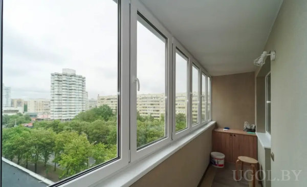 Эргономичный интерьер с табуретом, шкафом и видом на зелёные дворы и высотки.