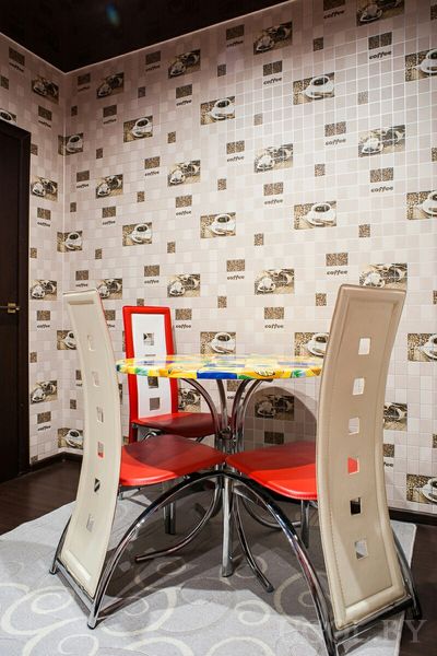 Круглый стол с жёлто-синей скатертью, красные стулья и кофейные мотивы на стенах, уютный уголок для завтраков.