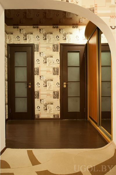 Два тёмных дверных полотна с матовым стеклом, обои с мотивами «MOVIE» и «HOLLYWOOD», зеркало и ковёр на фоне арки.