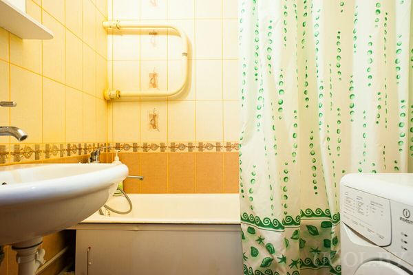 Стиральная машина, ванна, зелёная штора и плитка в жёлто-оранжевых тонах с декоративной вставкой.