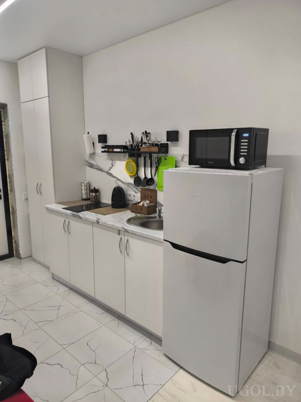 Современная кухня с белыми фасадами, чайником, сушкой и подвесными кухонными принадлежностями.