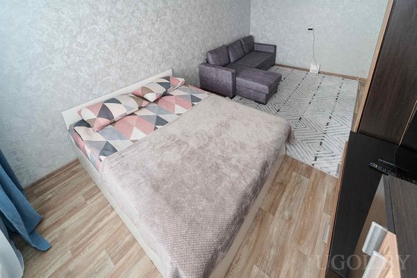 Комбинированная зона с кроватью в светлом текстиле, фиолетовым диваном и ковром с чёрно-белым узором.