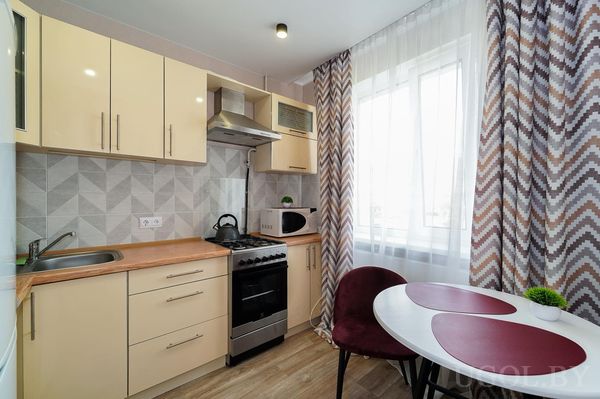 Компактная кухня с серым фартуком, деревянной столешницей, круглым столом и шторами с зигзагами.