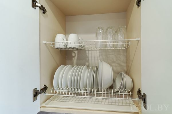Кухонный шкаф с сушилкой, белыми чашками, стаканами и аккуратно расставленными тарелками.