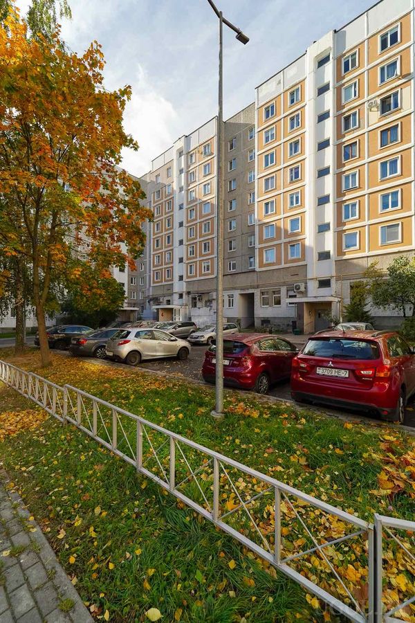 Городской двор с многоэтажкой, машинами, фонарём и деревьями с жёлтой листвой.