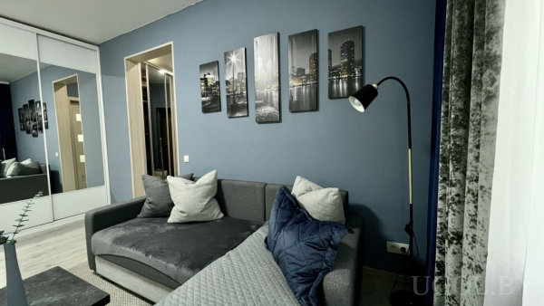 Синяя акцентная стена с пятью чёрно-белыми полотнами, торшер, серый диван и зеркальный шкаф-купе.