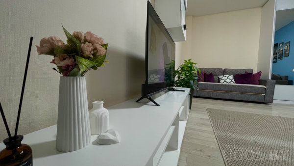 Белая тумба с декором: вазы, диффузор, диван с подушками, зелёное растение и зеркальный шкаф на фоне.