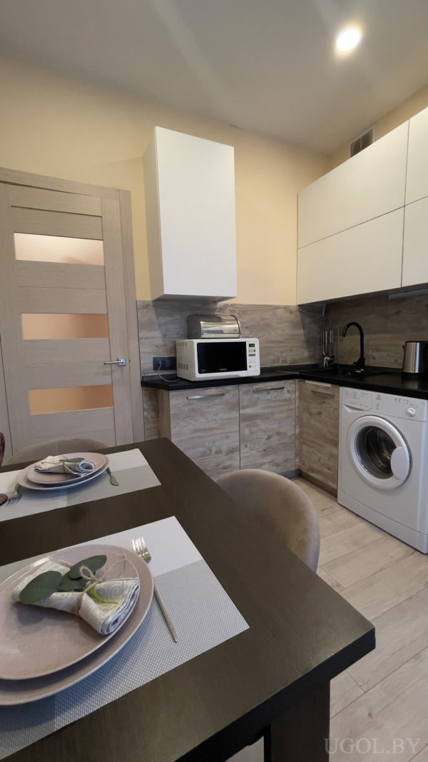 Светлая кухня с чёрной столешницей, сервированный стол на двоих, микроволновка, тостер и стиральная машина.