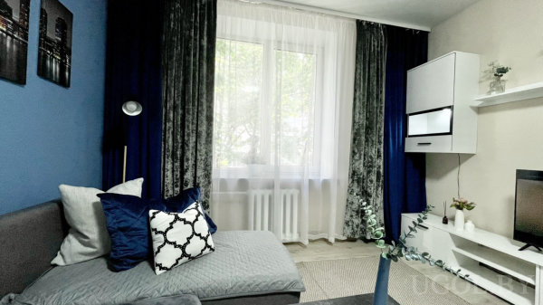 Серый секционный диван, синие портьеры и три городских постера, торшер и белая ТВ-зона создают современный стиль.