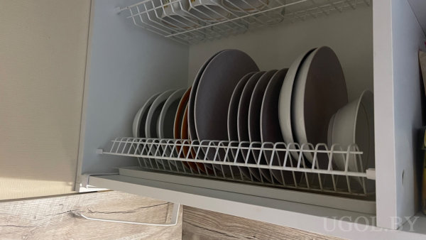 Вертикальная сушка с разноцветными тарелками, пустая верхняя полка, открытая дверца с деревянной текстурой.