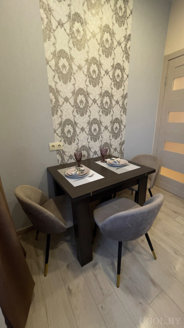 Тёмный стол на фоне серых обоев, сервировка на двоих, серые стулья с золотыми ножками, дверь с матовыми вставками.