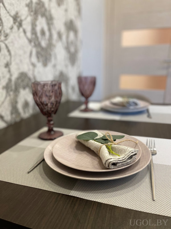 Сервированный стол: тарелки, салфетки с листьями, фиолетовые бокалы, фон с цветочными обоями и дверью.