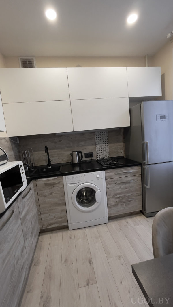 Светлое дерево на полу, серые нижние и белые верхние шкафы, чёрная столешница с мойкой, микроволновка и декоративная вставка на фартуке.