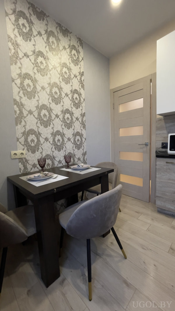 Стол на двоих, мягкие серые кресла с золотыми наконечниками, декоративная полоска обоев и светлый пол.