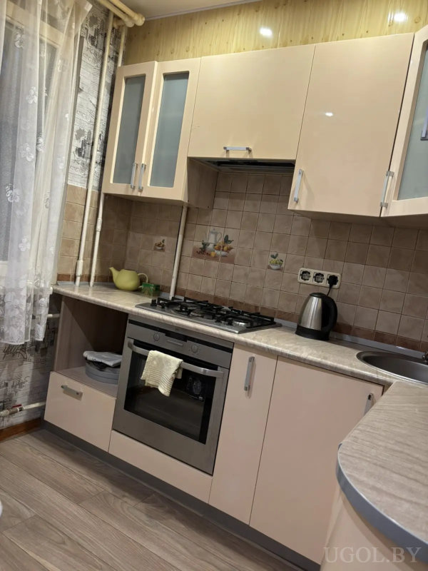 Бежевая кухня, плита, чайник, плитка с фруктами, тюль с цветами на окне.