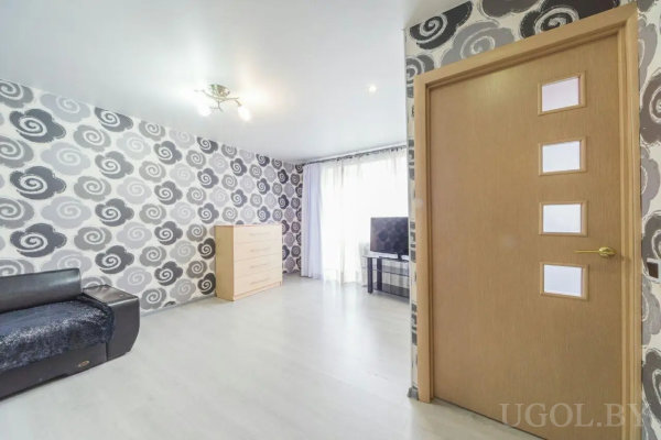 Современная комната с черно-белыми обоями, черным диваном, светлой мебелью и телевизором у окна.