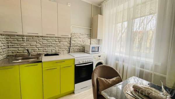 Зелёные и деревянные шкафы, плита, мойка, микроволновка, стеклянный стол с сервировкой.