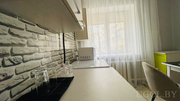 Белая столешница, три бокала на салфетке, стеклянная миска, кирпичный фартук и зелёный ящик.