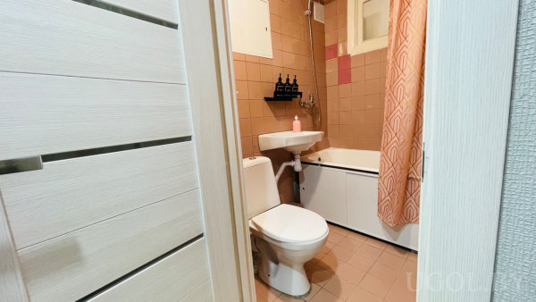 Унитаз, раковина, ванна с геометрической занавеской, полка с чёрными флаконами и мыльница.