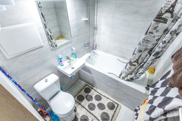 Белая сантехника, светло-серая плитка, занавеска с «Эйфелевой башней» и коврик в горошек. Всё организовано для удобства и чистоты.