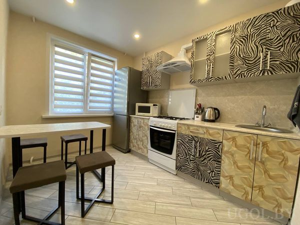 Необычная кухня с фасадами под зебру и жирафа, плитой, холодильником и обеденной зоной со столом и табуретами.