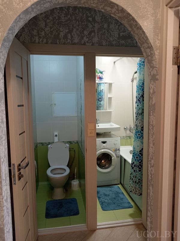 Компактная ванная с унитазом, стиральной машиной, раковиной и ванной с голубой шторой.