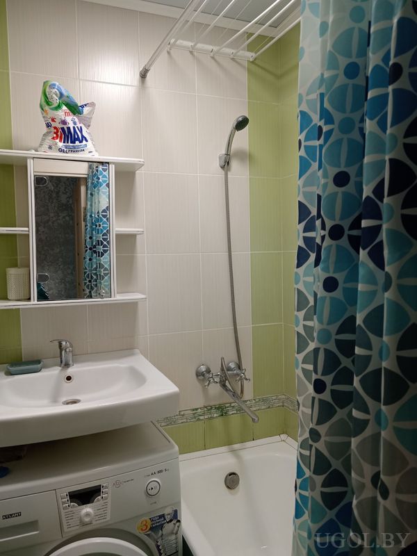 Небольшая ванная с раковиной, зеркалом, стиральной машиной и ванной с голубой шторой.