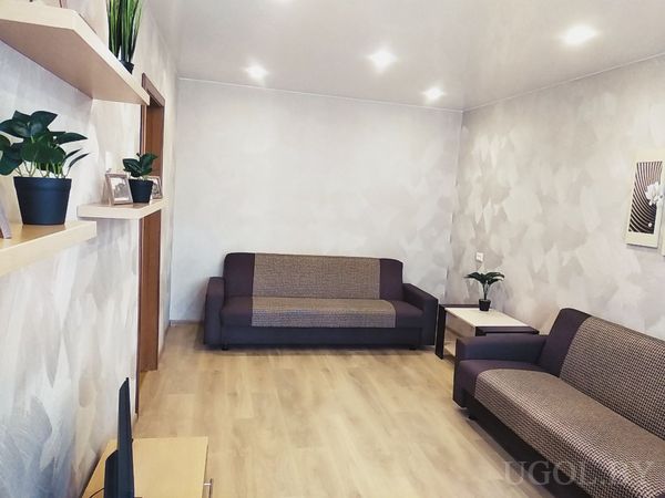 Современная гостиная с двумя диванами коричнево-бежевого цвета, журнальным столиком и зелёными растениями на полках.