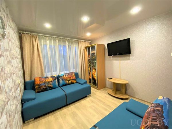 Яркая гостиная с синим диваном и пуфом, шкафом с фотопечатью города и телевизором на стене.