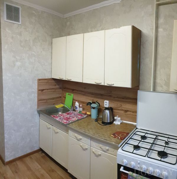 Компактная кухня с кремовыми шкафами, деревянным фартуком, мойкой, плитой и предметами на столешнице.