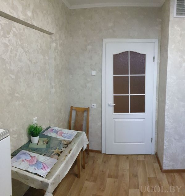 Небольшой уголок с белой дверью с коричневым стеклом, деревянным стулом и столом с зелёным растением и морскими подставками.